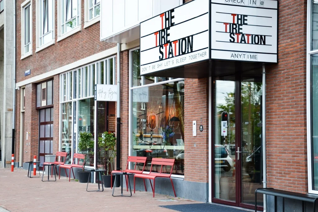 Street-level entrance with distinctive signage and red outdoor seating at Conscious Hotel City Hub in Amsterdam