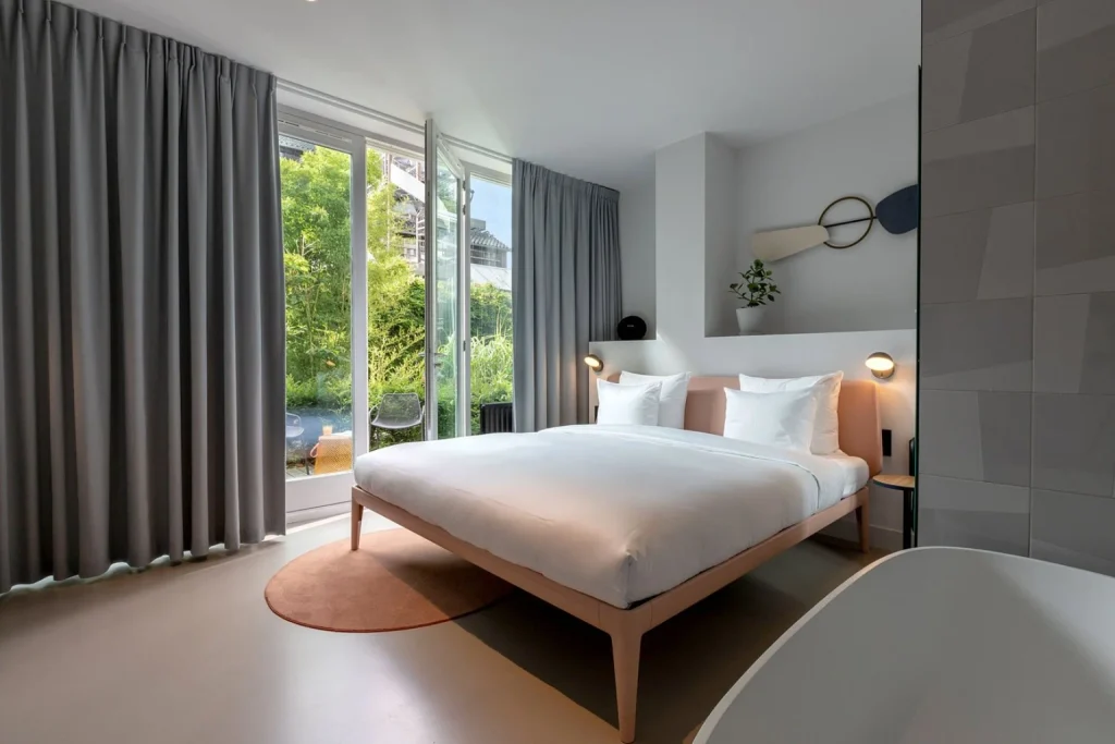 Contemporary guest room with a double bed, floor-to-ceiling windows and views of a leafy garden at Conscious Hotel Museum Square, Amsterdam