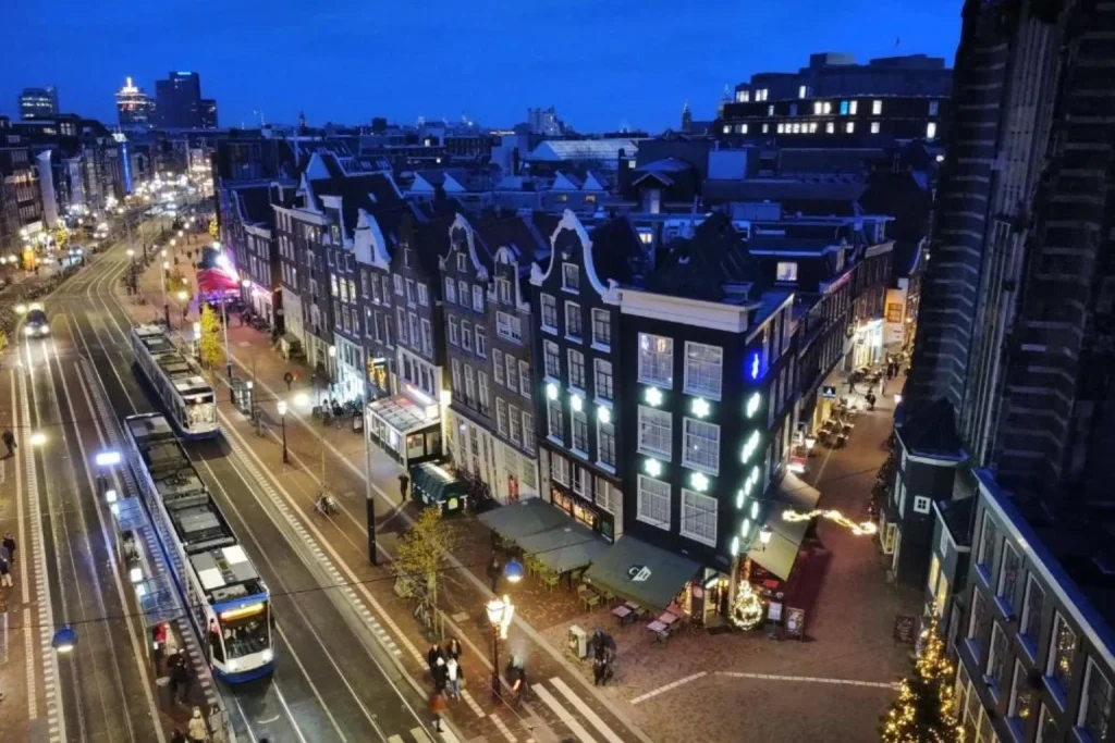 Evening city view around Corner House Amsterdam, with historic Dutch buildings, illuminated streets and trams in central Amsterdam.