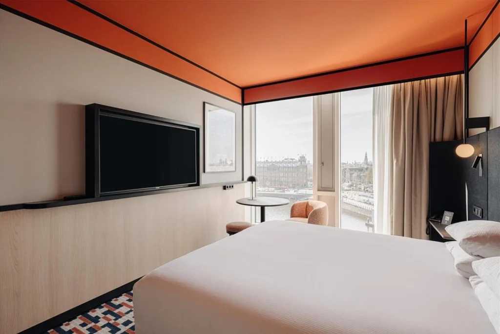 Modern hotel bedroom with king-size bed, contemporary orange ceiling, large TV and panoramic city views at DoubleTree by Hilton Amsterdam Centraal Station
