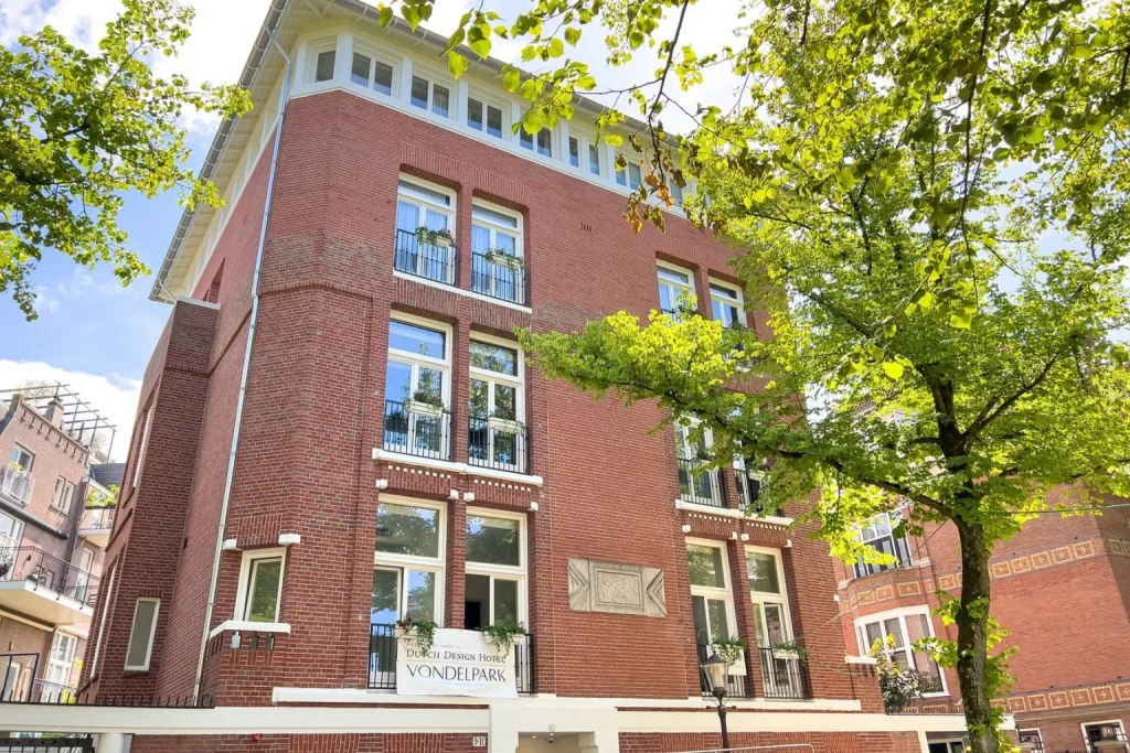 Historic red-brick façade with tall windows and leafy surroundings at Dutch Design Hotel Vondelpark in Amsterdam