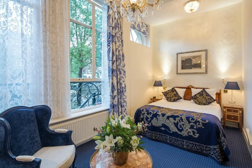 Elegant bedroom with blue patterned décor, chandelier and large canal-facing windows, Ambassade Hotel, Amsterdam