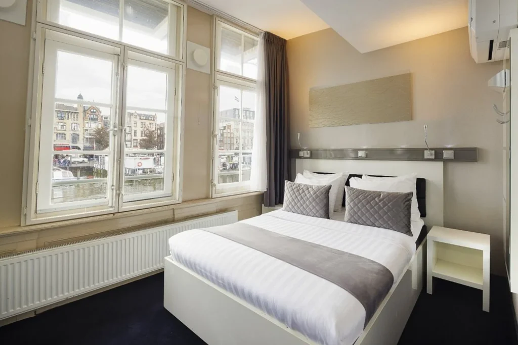 Bright double hotel room with comfortable bed, modern furnishings and large windows overlooking an Amsterdam canal at Hotel CC in Amsterdam