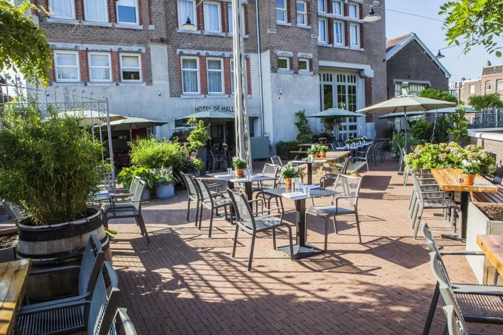Spacious outdoor terrace with dining tables, umbrellas and garden greenery at Hotel De Hallen, Amsterdam