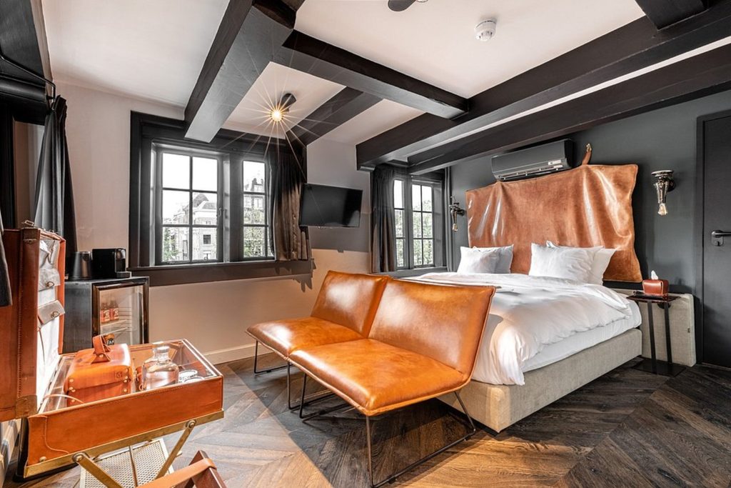Characterful luxury room with exposed ceiling beams, warm leather furnishings and large traditional windows at Hotel The Craftsmen in Amsterdam.