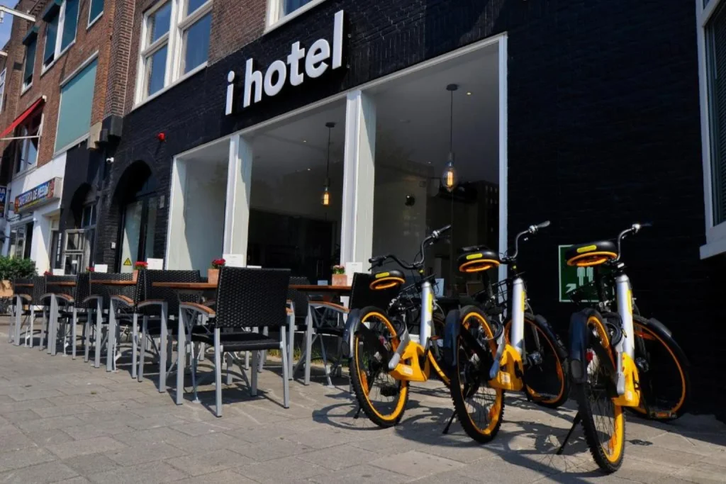 Street-level entrance with bicycles and outdoor terrace seating at I Hotel Amsterdam