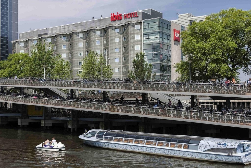 Waterfront view of ibis Amsterdam Centre with canal boats and extensive bicycle parking in central Amsterdam