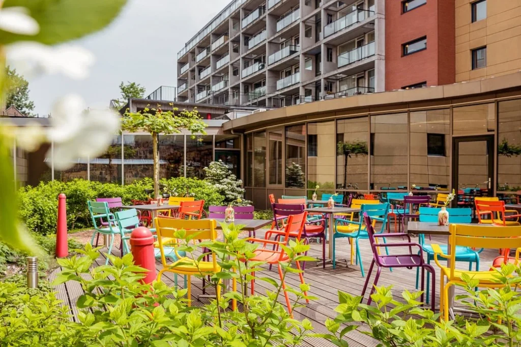 Colorful outdoor terrace with vibrant chairs, dining tables and lush greenery at Ibis Amsterdam Centre Stopera.