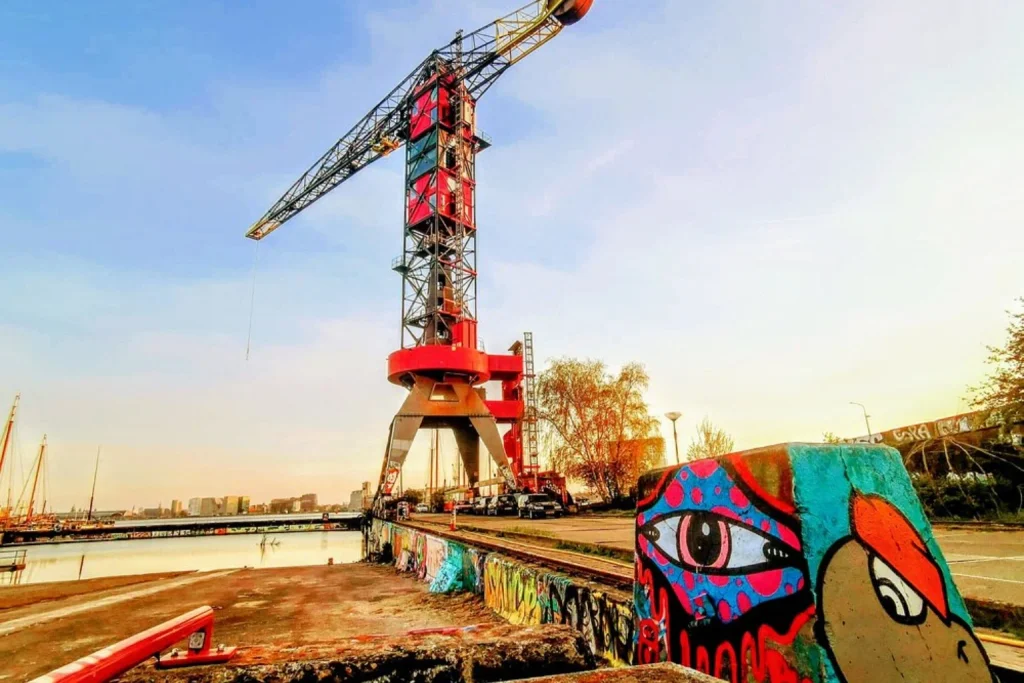 Iconic red harbour crane rising above colourful street art on Amsterdam’s industrial waterfront, Crane Hotel Faralda Amsterdam