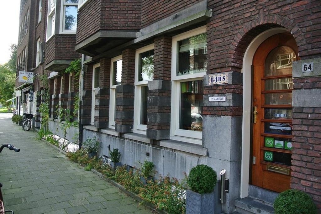 Traditional brick exterior with a wooden entrance and street-side greenery at InnAmsterdam4u B&B in Amsterdam