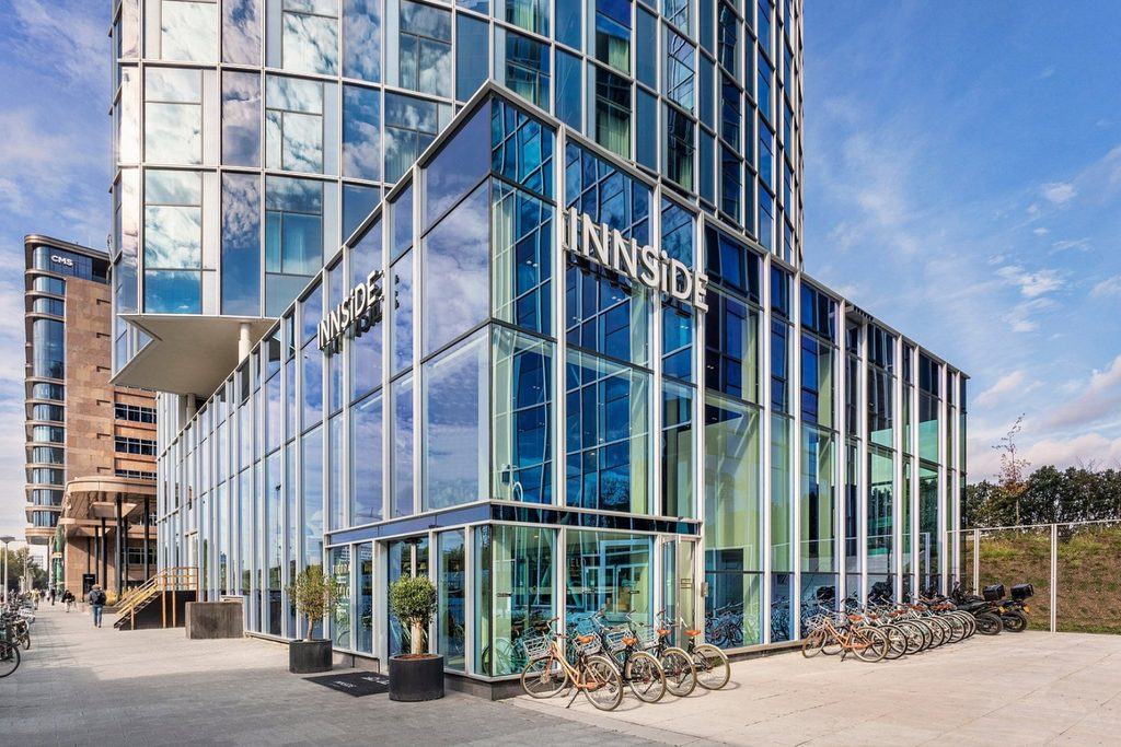 Contemporary glass façade and main entrance with bicycles parked outside at INNSiDE by Meliá Amsterdam
