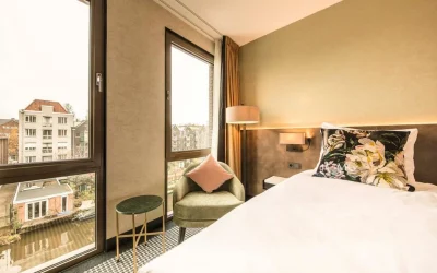 Modern boutique hotel room with comfortable double bed, floral cushions, cozy armchair and large windows overlooking an Amsterdam canal at Monet Garden Hotel Amsterdam