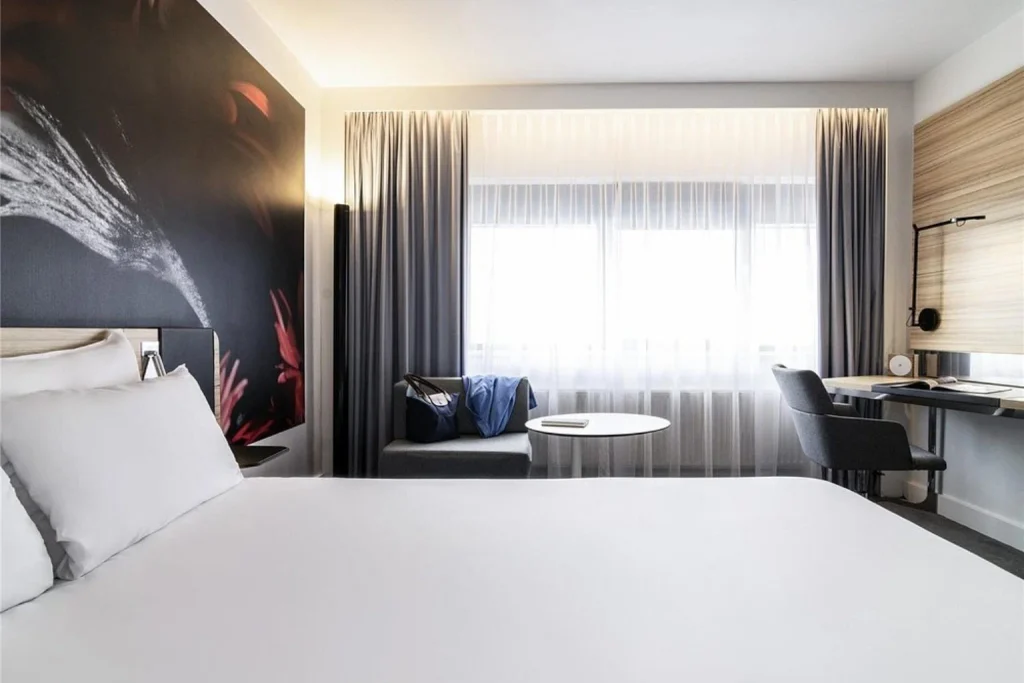 Contemporary guest room featuring a comfortable bed, large window, seating area and dedicated workspace at Novotel Amsterdam City, Amsterdam