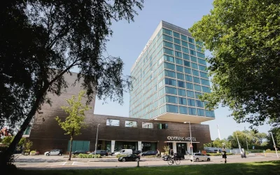 Contemporary high-rise hotel building with a glass façade and green surroundings near the Olympic Stadium at Olympic Hotel Amsterdam