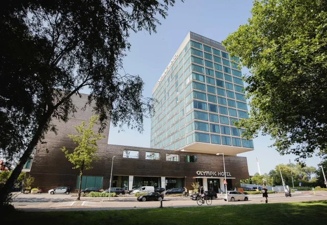 Contemporary high-rise hotel building with a glass façade and green surroundings near the Olympic Stadium at Olympic Hotel Amsterdam