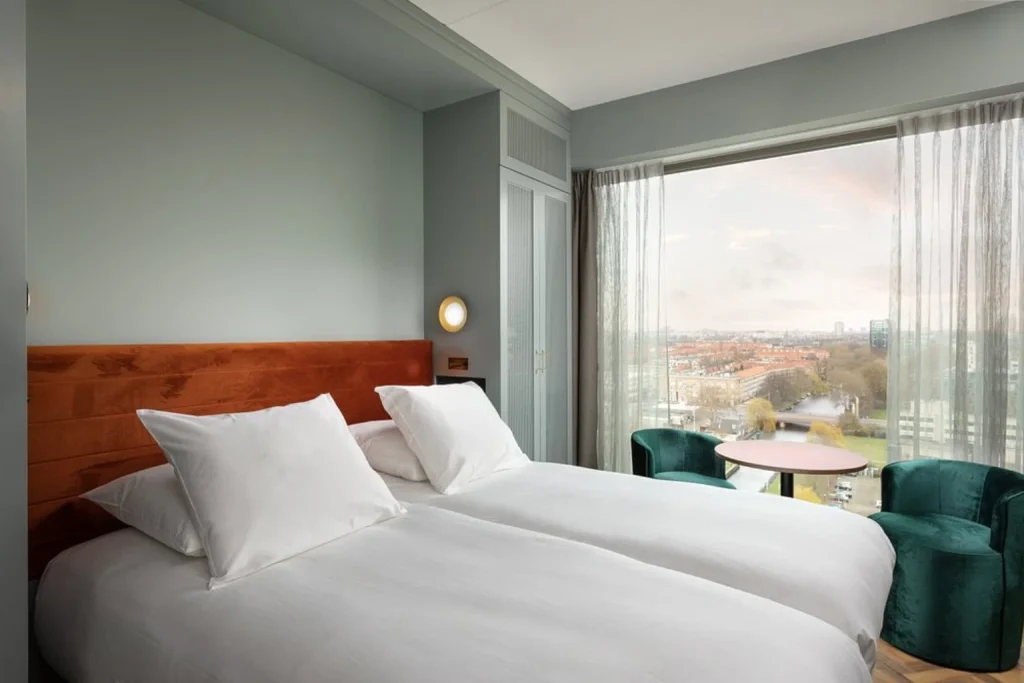 Bright contemporary twin room with floor-to-ceiling windows and panoramic views across Amsterdam at Olympic Hotel Amsterdam, Amsterdam