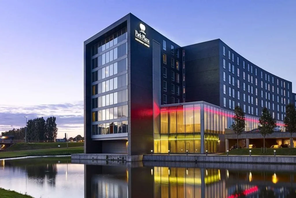 Modern airport hotel exterior with illuminated glass facade and waterfront setting at Park Plaza Amsterdam Airport in Amsterdam
