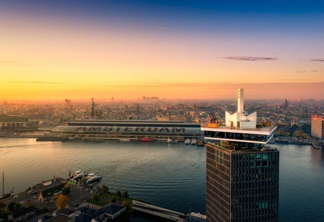 Aerial view of Sir Adam Hotel (A’DAM Tower) with Amsterdam skyline and waterfront at sunset
