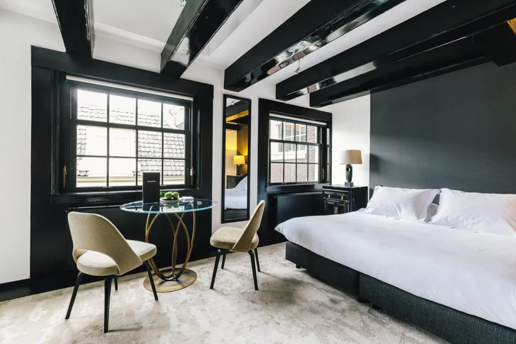 Stylish bedroom with exposed black ceiling beams, large windows and contemporary furnishings, The Dylan Amsterdam
