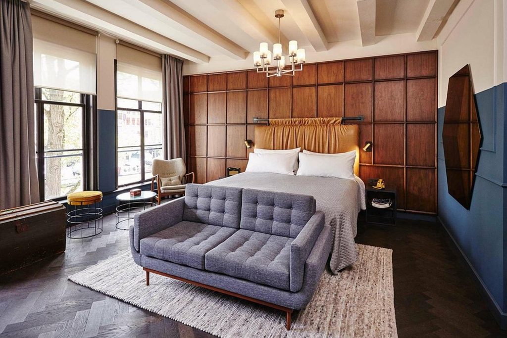 Stylish guest room with a large bed, grey sofa and warm wood-panelled walls at The Hoxton, Amsterdam