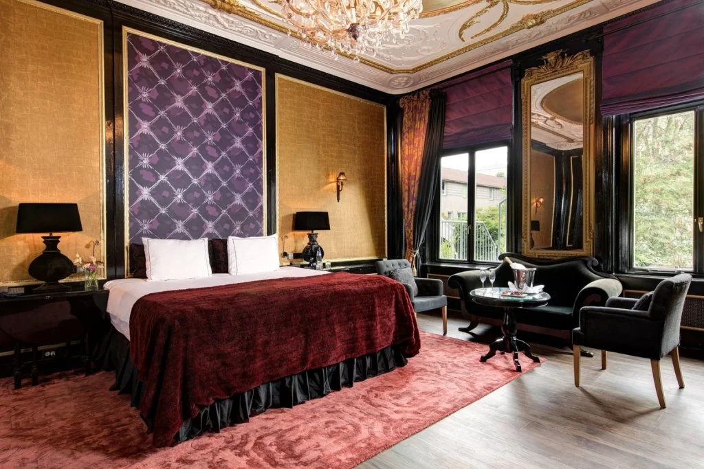 Luxury boutique hotel room with ornate gold décor, chandelier and elegant seating area at The Toren in Amsterdam