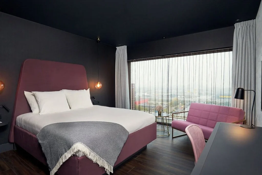Modern guest room with a large bed, pink furnishings and floor-to-ceiling city views at Van der Valk Hotel Amsterdam Amstel, Amsterdam