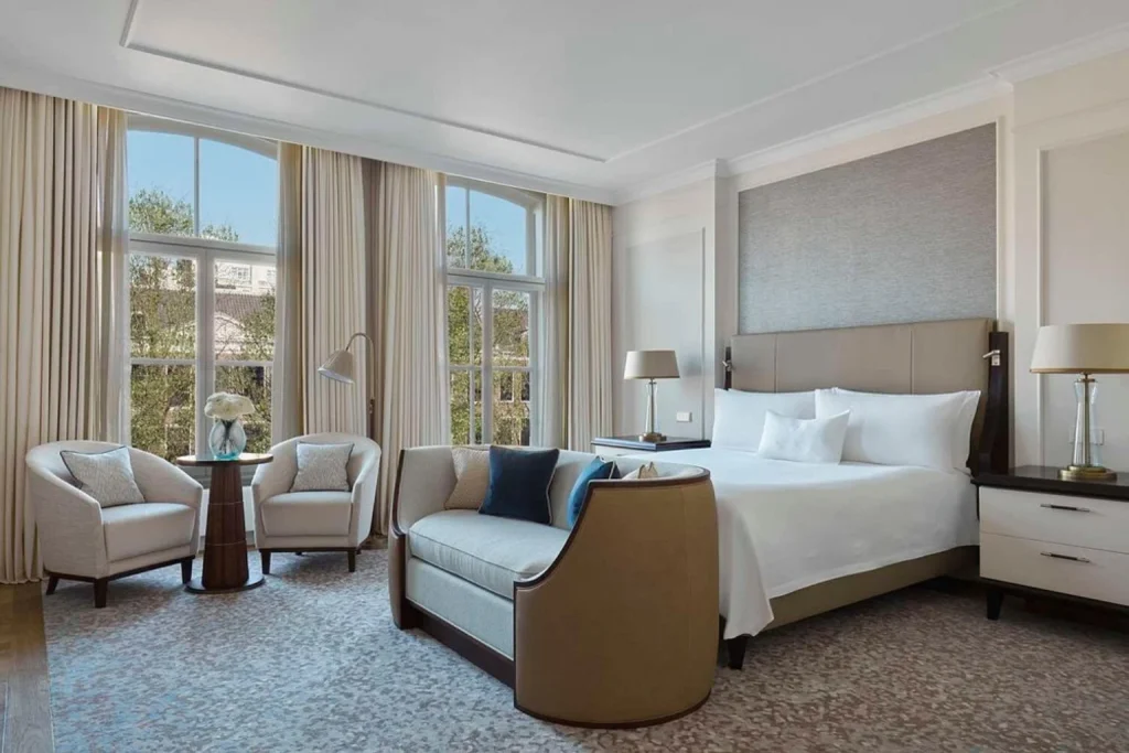 Spacious luxury suite featuring a king-size bed, refined furnishings, comfortable lounge seating and floor-to-ceiling curtains at Waldorf Astoria Amsterdam.